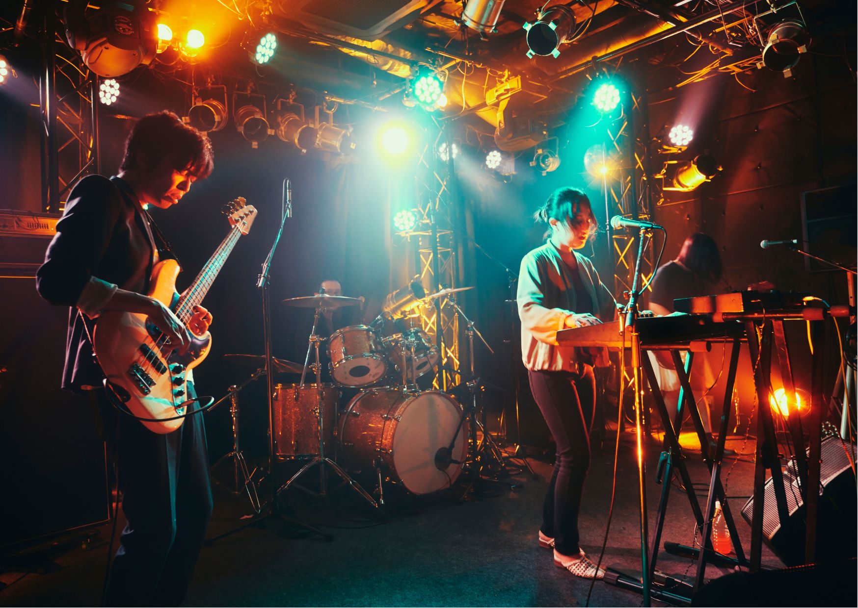 Musicians performing on stage with bassist, drummer, and keyboard players under bright orange, blue, and yellow stage lights.