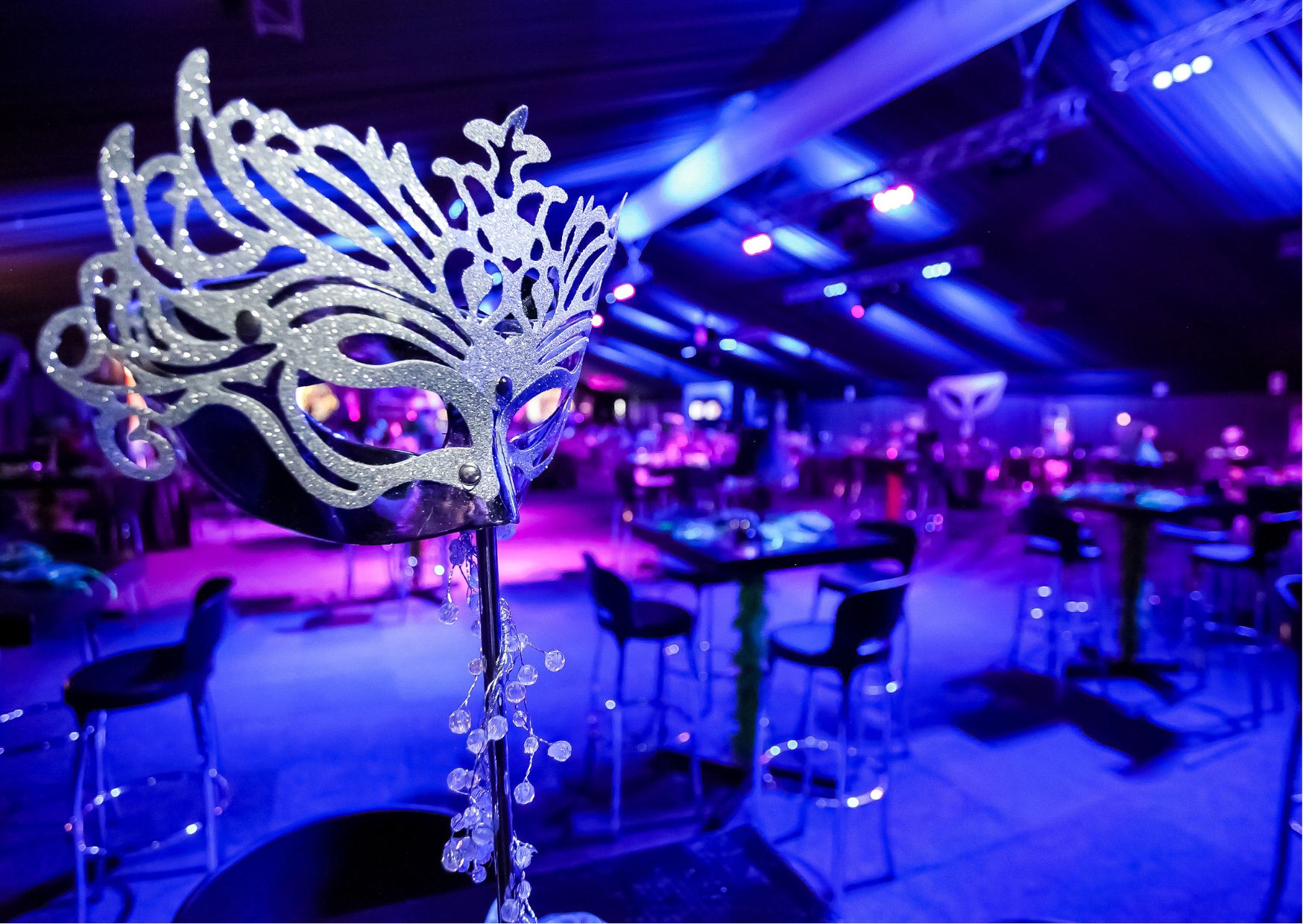 Glittering silver mask on stand with ballroom lit in purple and blue lighting.