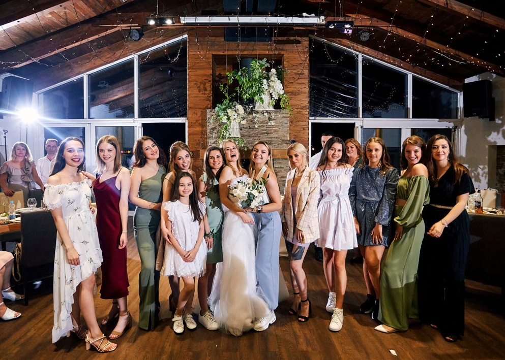 Bride with bouquet surrounded by bridesmaids and guests in various dresses at rustic industrial wedding venue