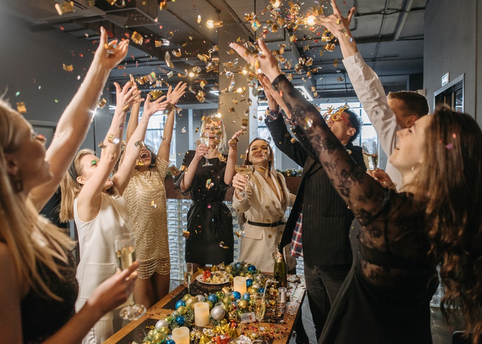 Group of friends tossing confetti in the air during indoor party celebration.