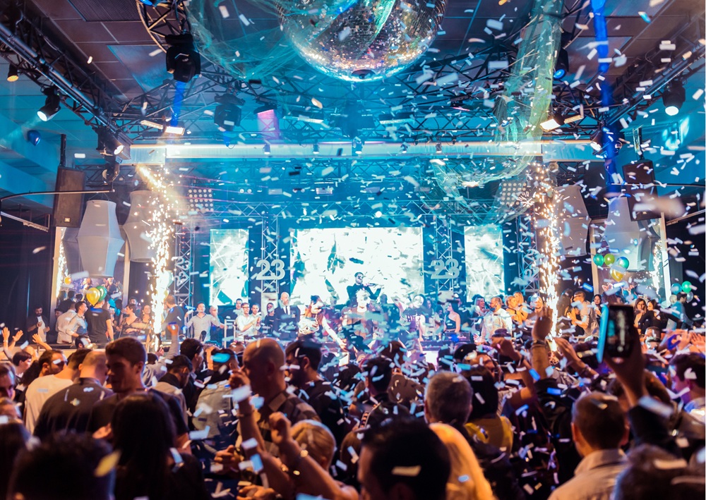 Indoor nightclub party with disco ball, confetti, pyrotechnics, and crowd dancing under lights.