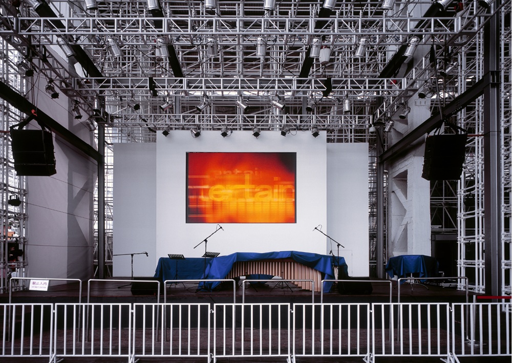Professional stage setup with metal truss system, lighting, and blue seating for event.