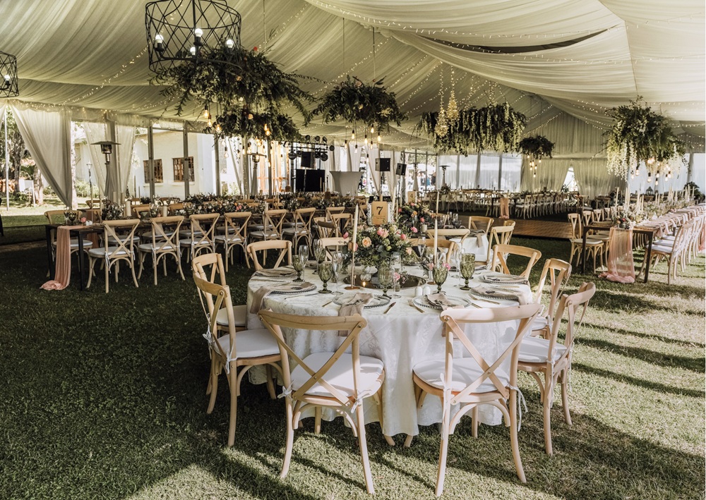 Elegant wedding tent with draped fabric, chandeliers, and rustic wooden chairs for formal dining.