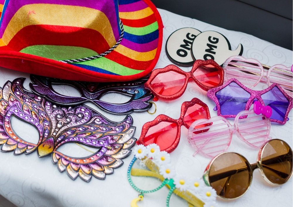 A table of vibrant glasses, masks, and hats ready for fun party photos.