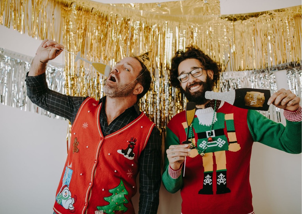 Two men celebrate with props under gold streamers during a holiday photo booth session.