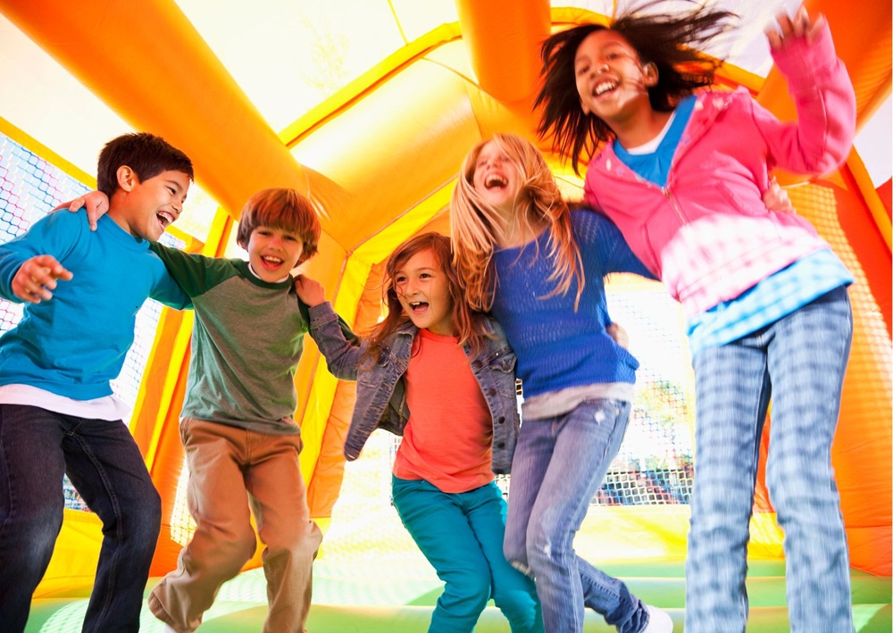 Happy children jump and laugh inside a brightly colored inflatable bounce house.