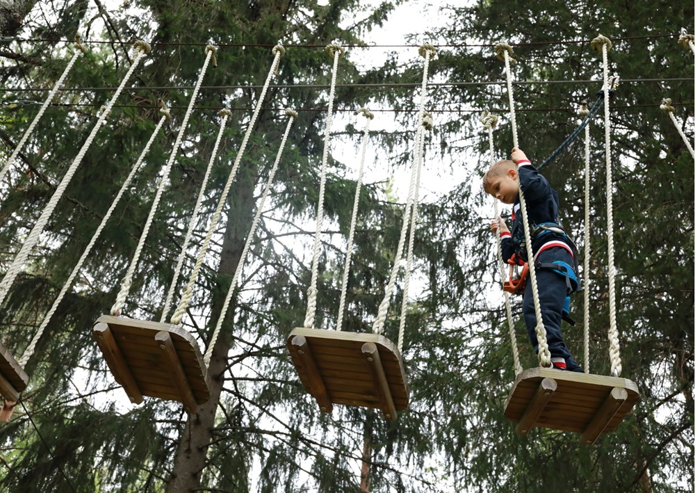 Young boy crosses hanging wooden platforms on a high ropes adventure course.
