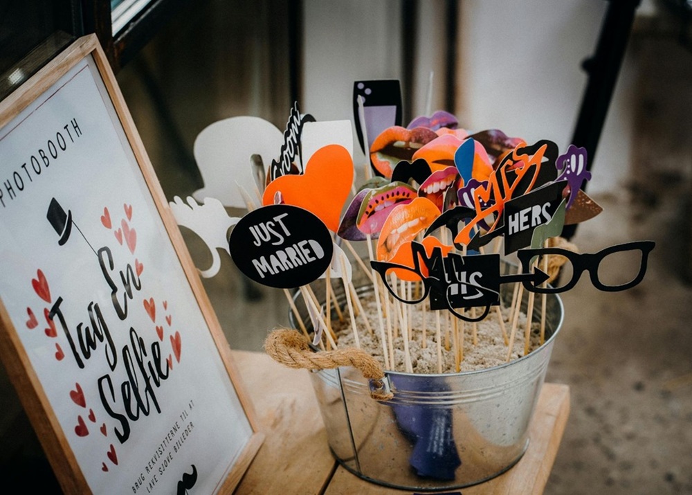 Wedding guests share playful props and signs beside a photo booth display.
