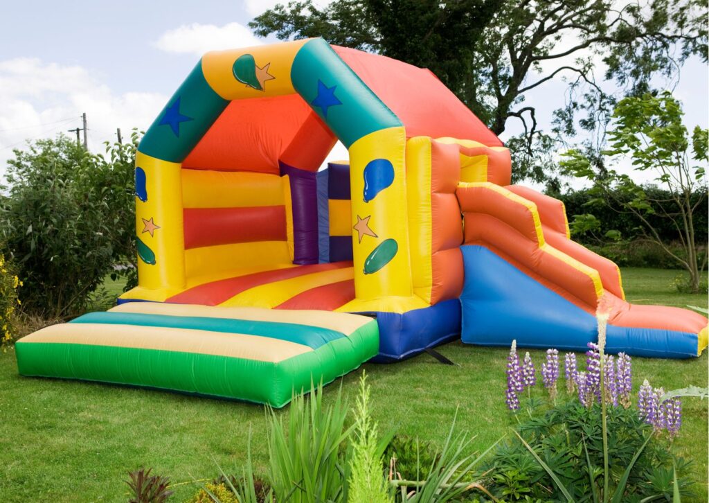 Bright inflatable bounce house with an attached slide sitting on a grassy lawn.
