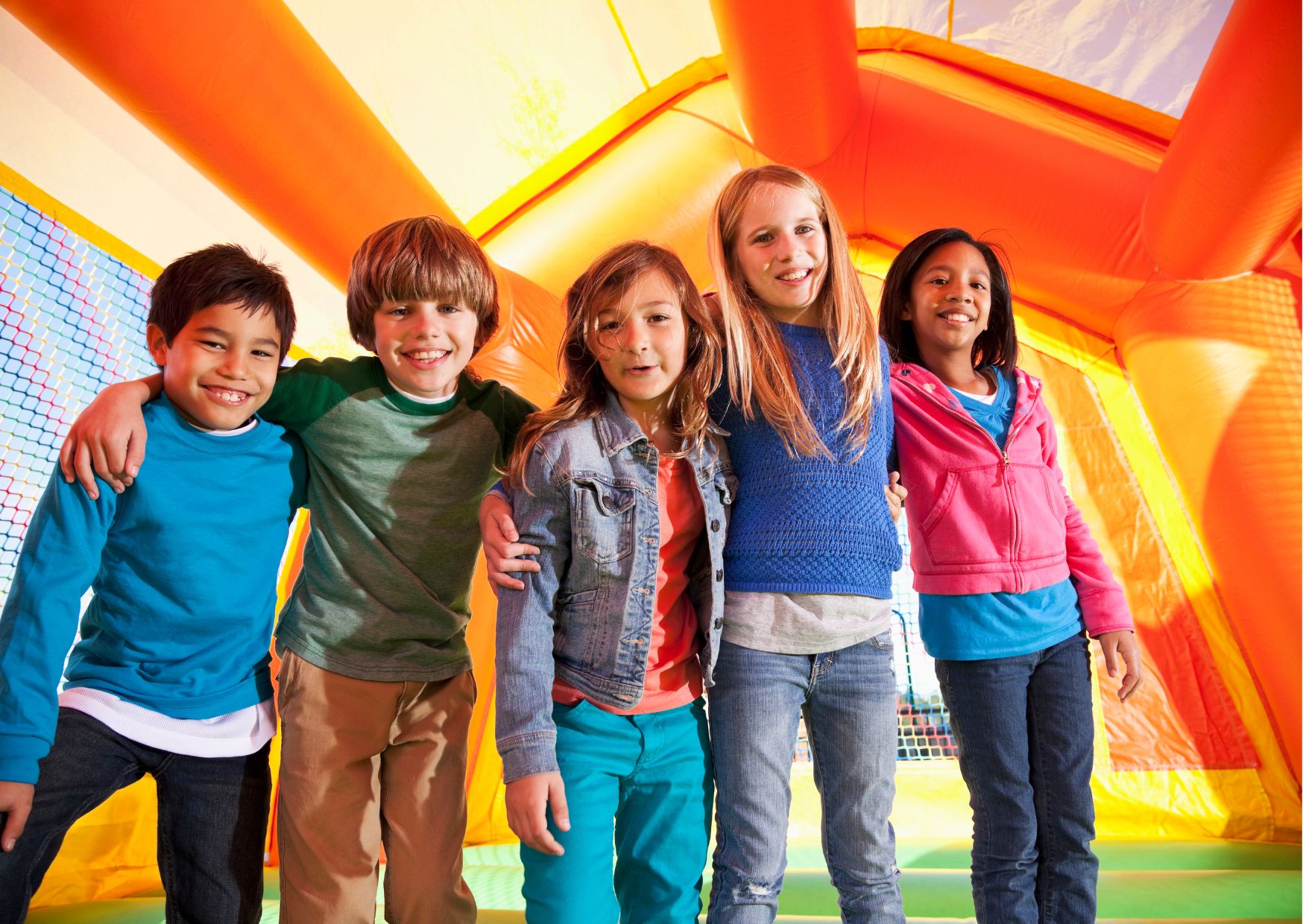 Five children smiling together inside a brightly colored inflatable bounce house.