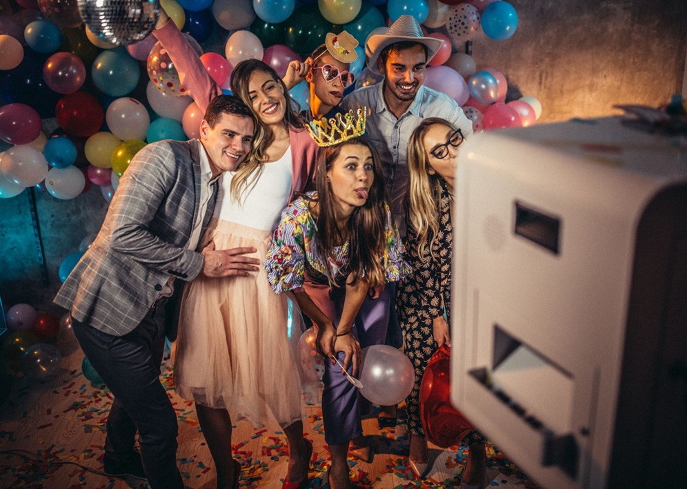 Friends pose for a festive photo booth picture at a Bar Mitzvah surrounded by balloons and colorful decorations.