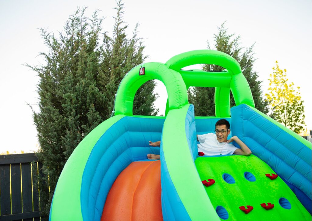 Child climbing a bright green and blue inflatable slide with colorful footholds.