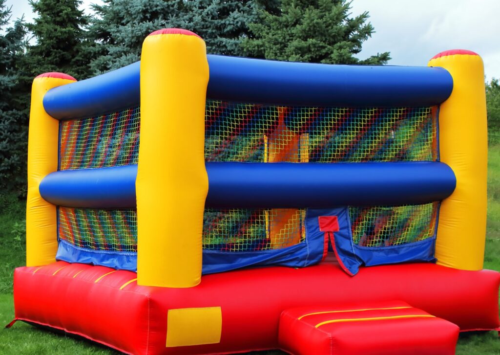Inflatable bounce house with safety netting, blue rails, yellow supports, and red flooring.