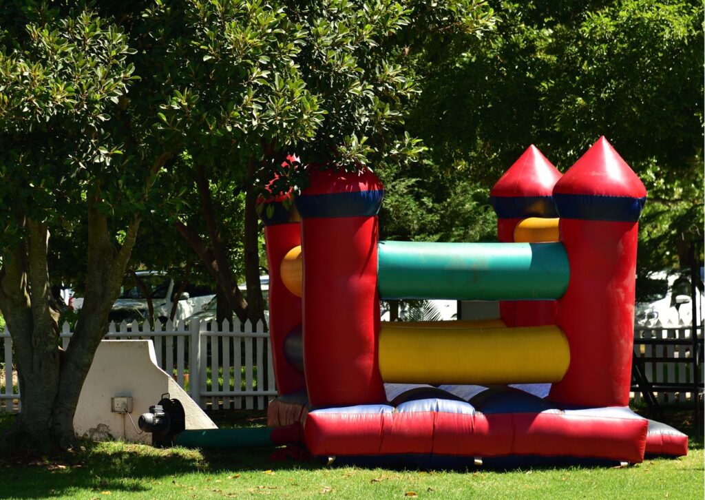 Red, blue, green, and yellow inflatable bounce house placed on grass beneath trees.