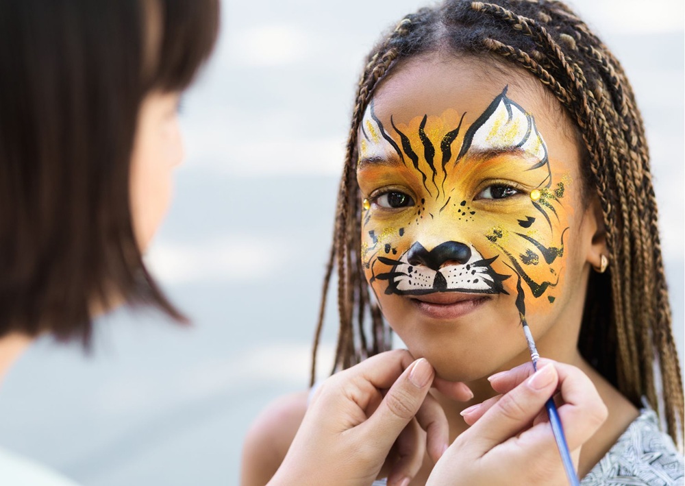 Face painter creates tiger makeup for a child, suggesting playful Bar Mitzvah entertainment activities.